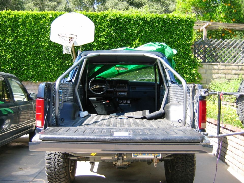 Rear of blue Ford Bronco with tailgate down, roll cage and exposed interior visible.