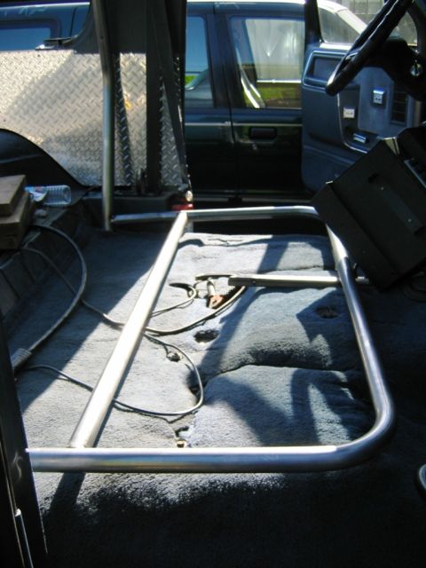 1985 Ford Bronco - The interior of a vehicle shows a newly installed roll cage with metal tubing and carpeting on the floor.