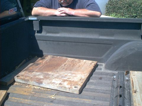 1966 Ford Bronco - A man leans over the edge of a truck bed containing a metal plate and wooden supports.