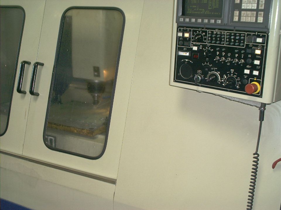 Control panel with buttons and dials mounted on a wall next to a machine with a window