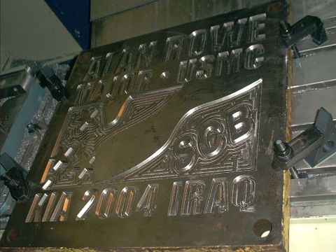 1966 Ford Bronco - Close-up of a steel memorial plaque clamped in a CNC mill, with raised machined lettering reading 'ALAN ROWE MAJOR · USMC' and 'KIA 2004 IR…