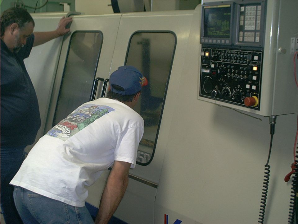 Two men look into the window of a large industrial machine with a complex control panel