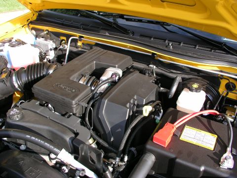 2005 Chevrolet Colorado - Engine bay of a yellow vehicle, showing the engine cover, battery, and various hoses and wires.