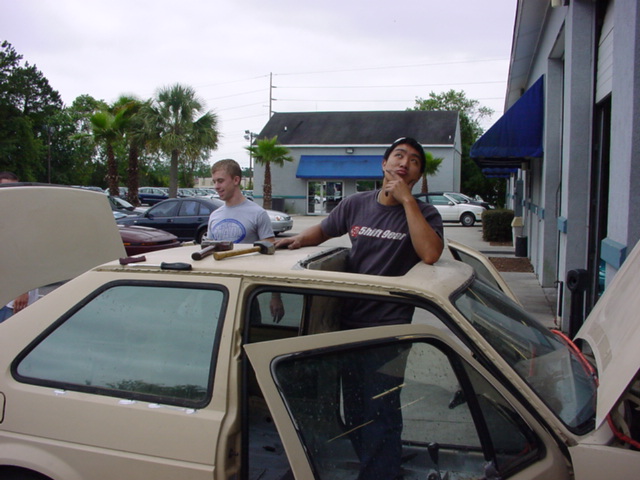 Two men working on the sunroof of a tan 1998 Volkswagen Jetta
