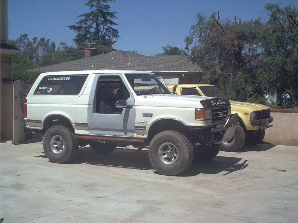 Lifted white Ford Bronco with black hood and door open on a driveway