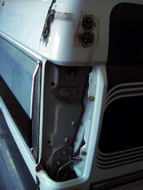 1994 Ford C-350 (Centurion Conversions) - The rear corner of a white truck shows rust and damage around the tailgate hinge area.