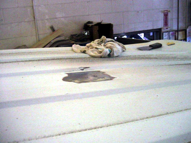 White vehicle roof with bare metal patch ground down for body repair, rag and spreader nearby