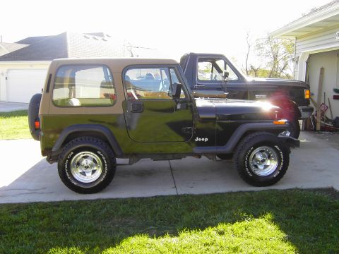 1995 Jeep Wrangler - A two-door Jeep Wrangler is parked beside a black pickup truck in a driveway.