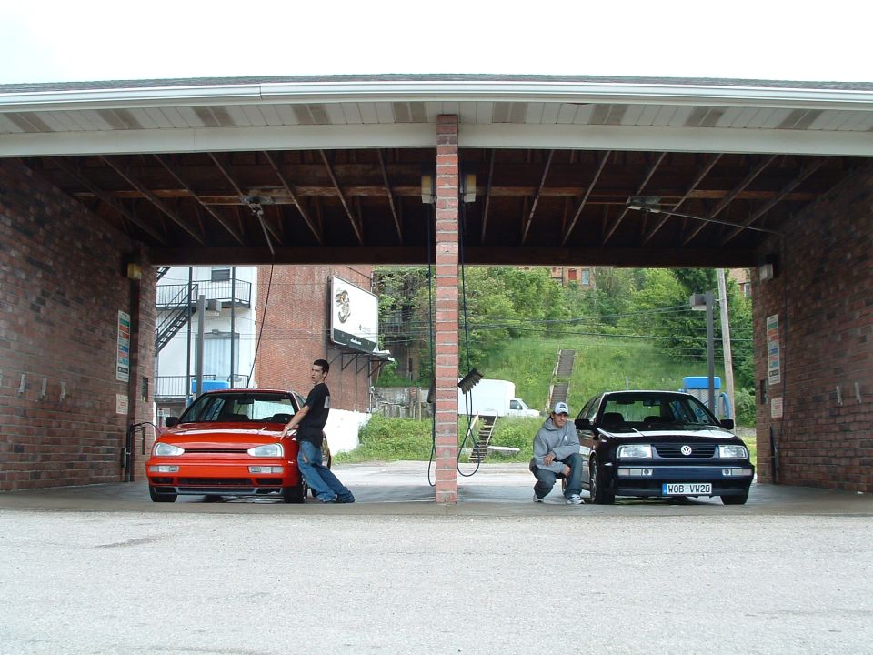 Two Volkswagen Jettas, one red and one dark blue, parked under a brick awning