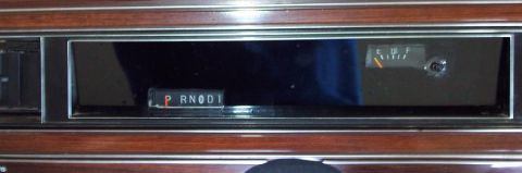 1985 Ford Crown Victoria LTD - The interior of a car shows the gear selector and a fuel gauge against a wood-grain trim.