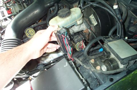 1999 Ford Crown Victoria - Close-up of a hand disconnecting a car's wiring harness in the engine bay.