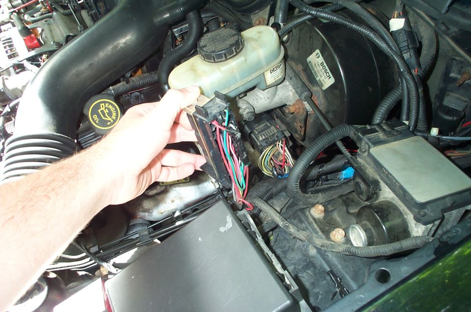 Hand disconnecting wiring harness in car engine bay near brake booster and air intake