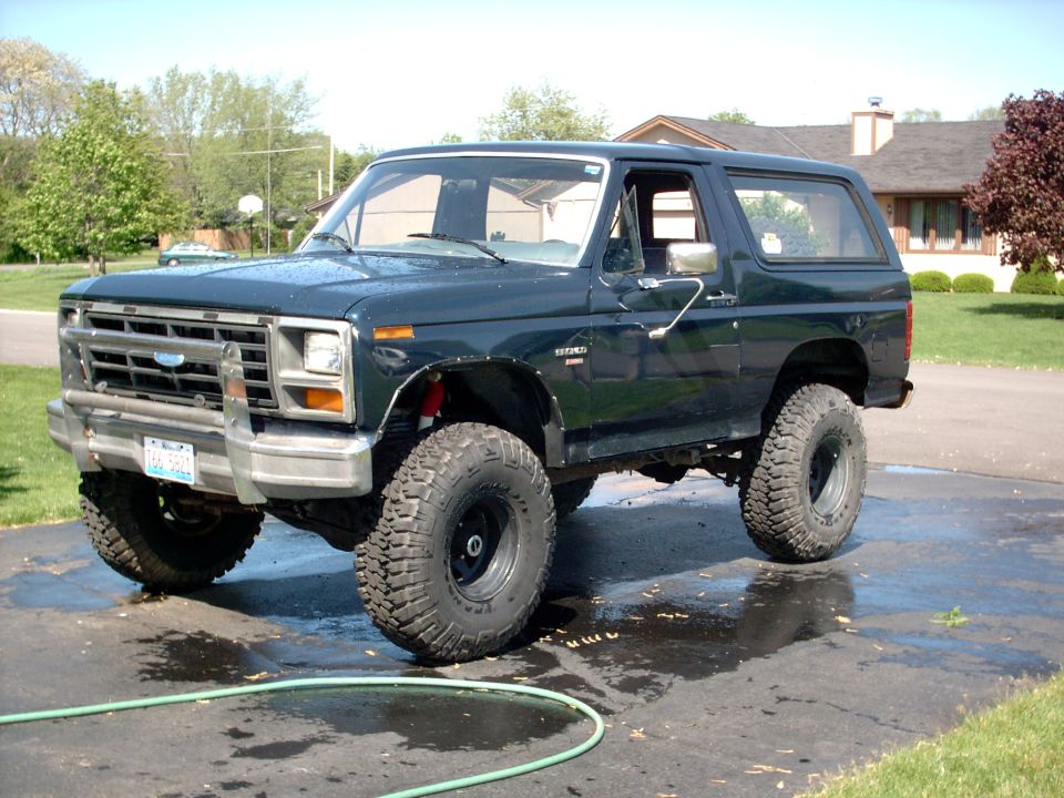 Dark green lifted Ford Bronco SUV on off-road tires parked on wet driveway
