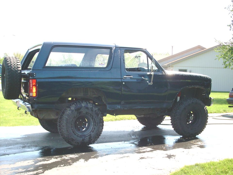 Dark blue lifted Ford Bronco with oversized off-road tires on wet driveway.
