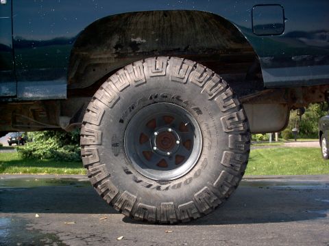 1986 Ford Bronco - Close-up side view of a Goodyear Wrangler MT/R mud-terrain tire mounted on a gray steel wheel with a 5-lug pattern, on a dark SUV. The vehi…