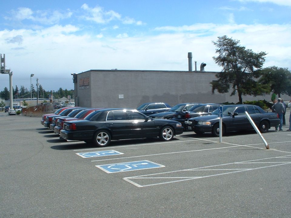 Black Ford Crown Victoria parked in a lot, side view, with other similar cars behind it