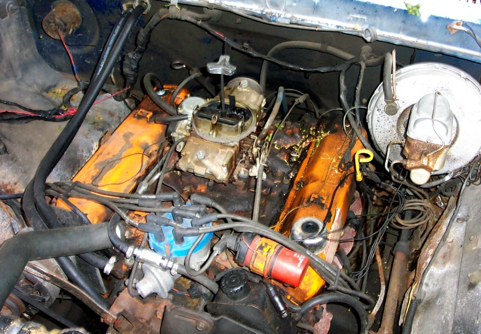 Tired V8 engine bay with carburetor, orange valve covers and heavy surface rust