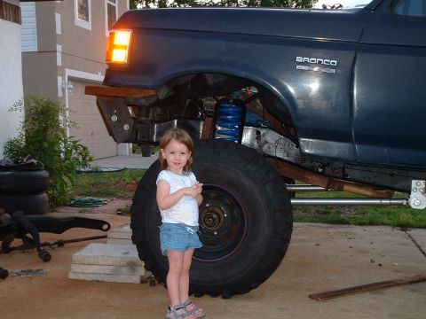 1995 Ford Bronco - A young girl poses next to a lifted Ford Bronco, its massive tires and suspension modifications.