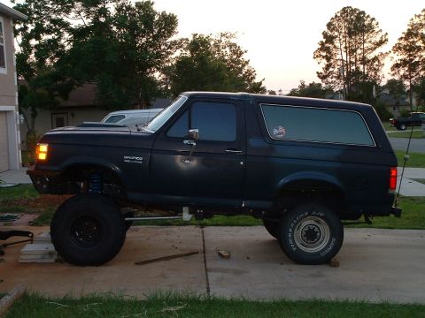 1995 Ford Bronco - A modified Ford Bronco sits on a driveway, its lifted suspension and large tires clearly visible.
