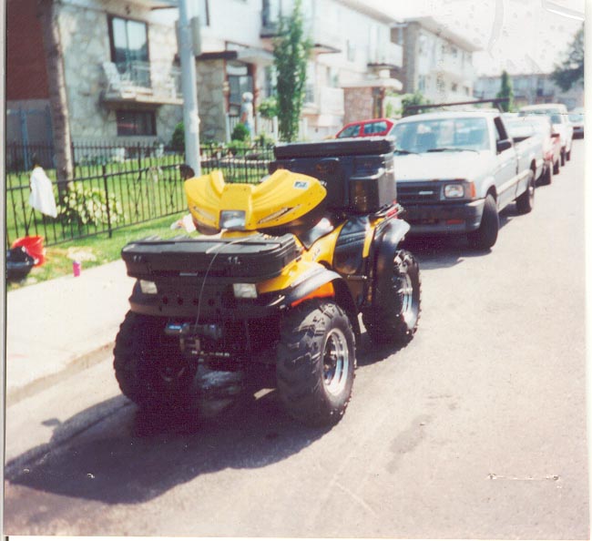 Yellow and black ATV parked at curb, rear 3/4 view, on residential street