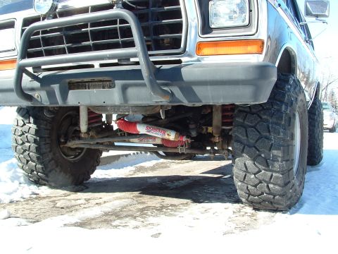 1979 Ford Bronco - This modified 1979 Ford Bronco features oversized tires and a prominent brush guard, with visible red shocks on the suspension.