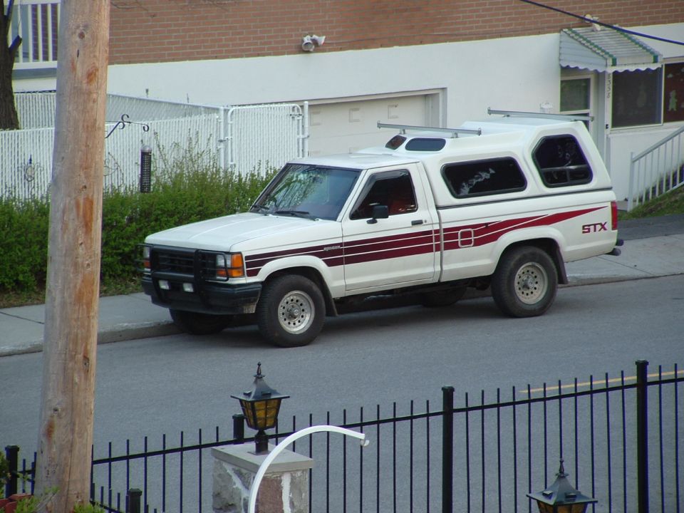 White Ford STX pickup with white camper shell and red stripes parked on a street by a brick house