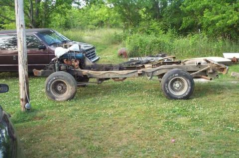 1979 Ford Bronco - The frame and engine of a vehicle sit in a grassy yard, with the body removed.