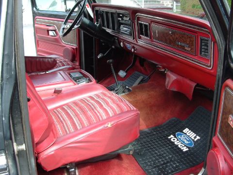 1979 Ford Bronco - The interior of this Ford Bronco shows a red dashboard and seats, with a "Built Ford Tough" floor mat visible.