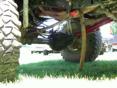 1985 Ford Bronco - The underside of a heavily modified truck is shown, with a focus on its off-road suspension and large tires.