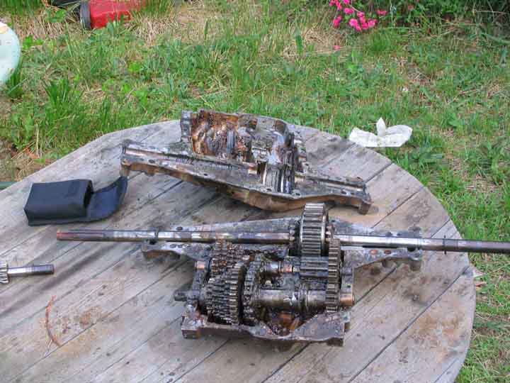 Disassembled greasy manual transmission halves and gear clusters on a wooden picnic table