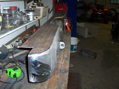 1994 Ford F-150 - A custom-fabricated metal bumper with a diamond plate top surface sits on a workbench in a garage.