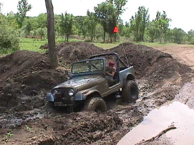 Jeep Wrangler driving through mud pit with a driver wearing a red hat