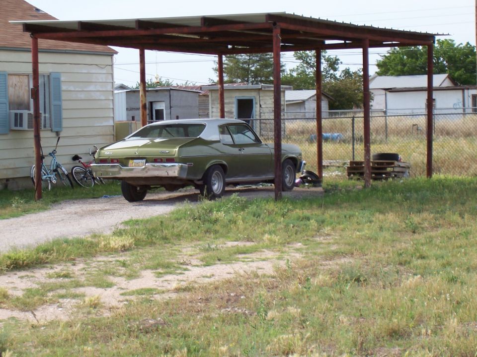 Green 1973 Chevrolet Nova coupe parked under a carport, rear view