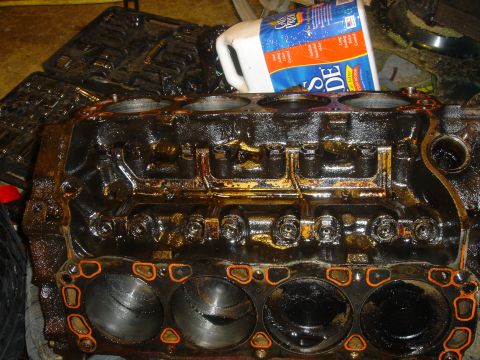 1986 Ford Mustang - Engine block with orange gasket material, covered in oil and grime, with a bottle of cleaning fluid in the background.