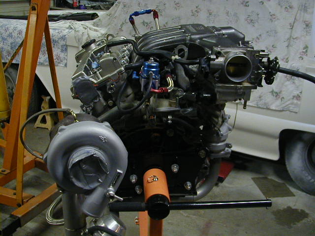 Turbocharged V6 engine on an orange engine stand with AN fittings and open throttle body