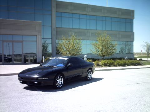 1995 Ford Probe - A black coupe is parked in front of a glass-windowed office building on a sunny day.
