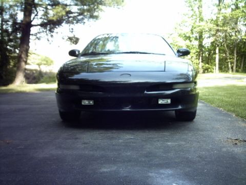 1995 Ford Probe - A black 1995 Ford Probe is shown from the front, parked on a driveway with trees and grass visible.