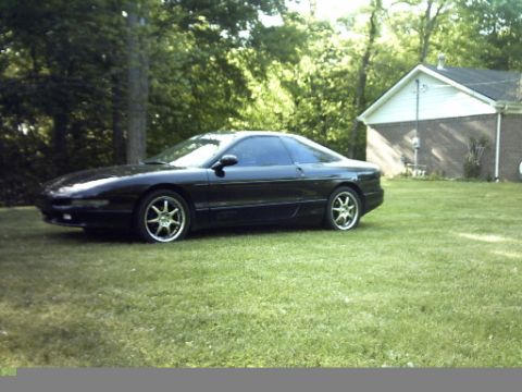 1995 Ford Probe - A black 1995 Ford Probe is parked on a lawn in front of a house, with trees in the background.