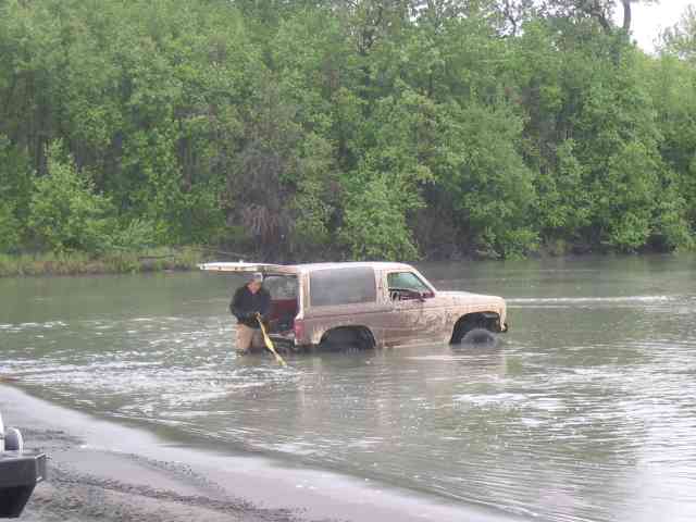 Tan SUV partially submerged in water, person standing by open rear door