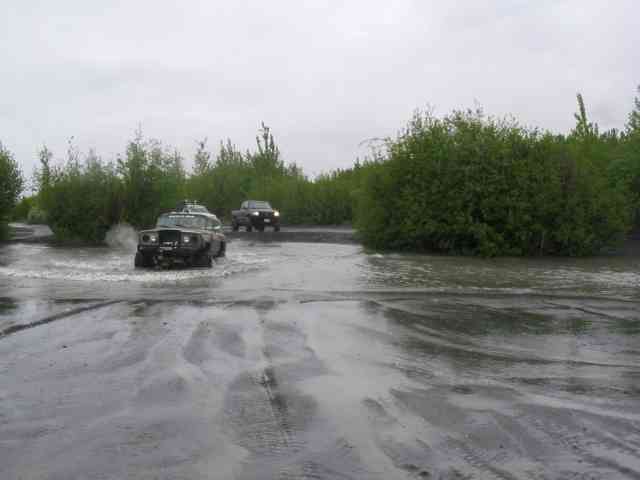Two off-road vehicles driving through a flooded area with trees on the sides