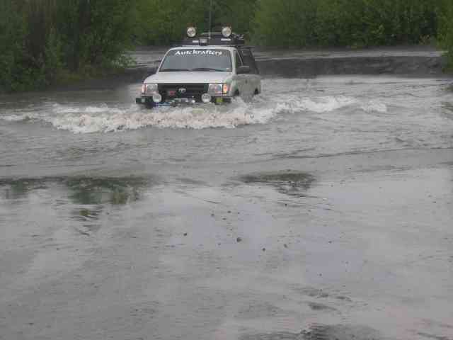 White SUV with roof rack and lights driving through water