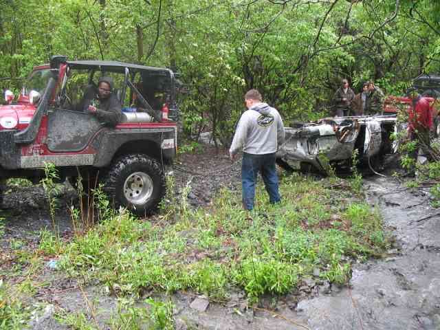 Red Jeep Wrangler next to a wrecked white vehicle in a wooded area