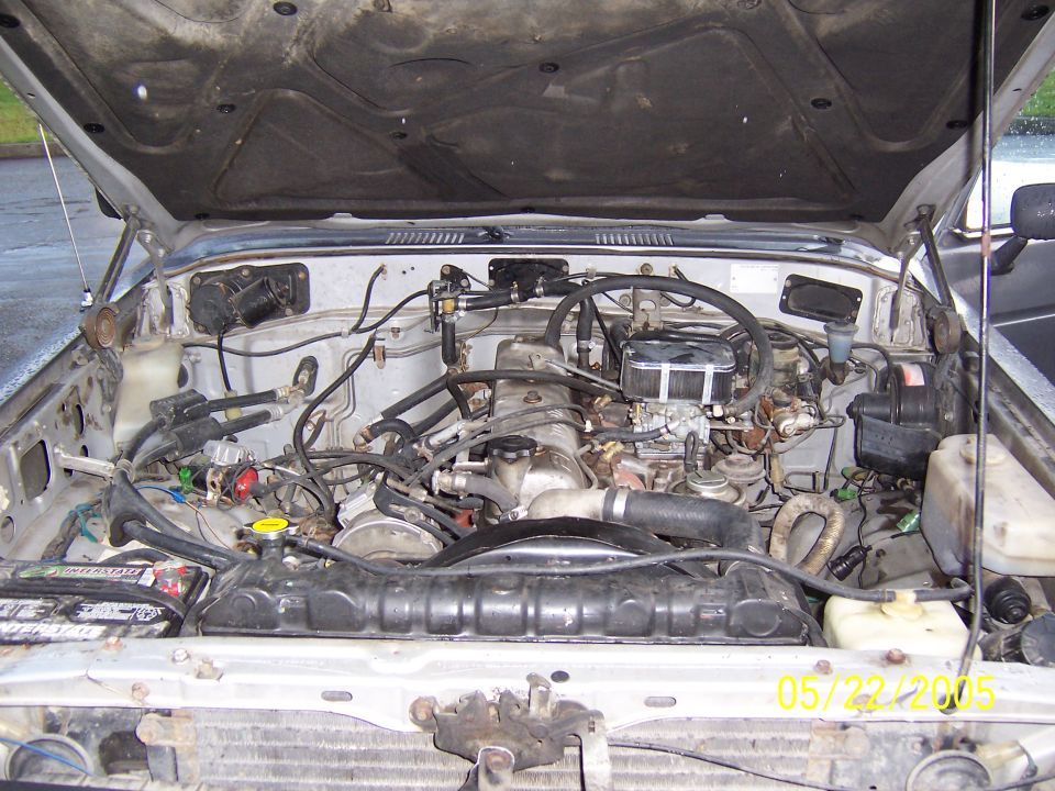 Engine bay of a silver Toyota Land Cruiser with hood open, showing engine and hoses