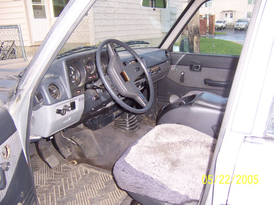 Gray interior of Land Cruiser with steering wheel, manual shifter and sheepskin seat cover