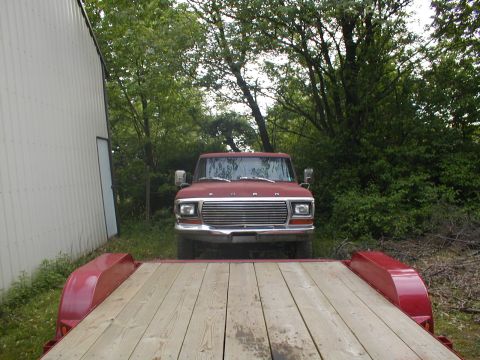 1979 Ford Bronco - A red 1979 Ford Bronco is parked in front of a building, viewed from the bed of a trailer.