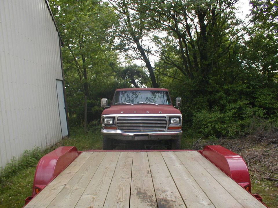 Front view of a red 1979 Ford Bronco parked near a building with trees in the background