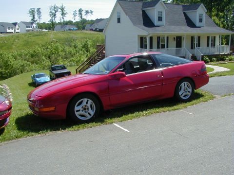 1994 Ford Probe - A red 1994 Ford Probe is parked on the lawn next to a driveway, with a house and other cars in the background.