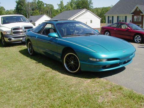 1994 Ford Probe - A teal Ford Probe is parked on a grassy lawn next to a white pickup truck and a red car.