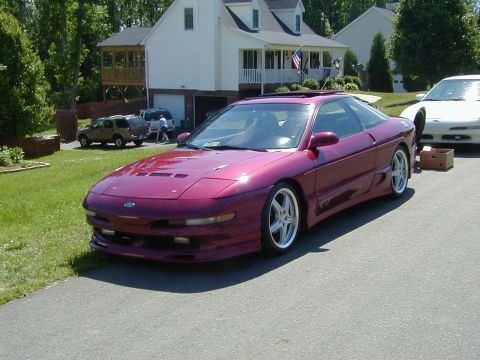 1994 Ford Probe - A maroon 1994 Ford Probe is parked in front of a house, with another white car visible behind it.