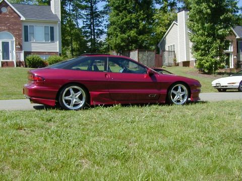 1994 Ford Probe - Side view of a red 1994 Ford Probe GT with custom wheels, parked near houses.